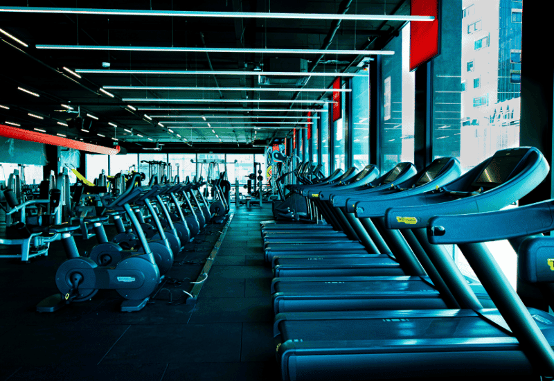 Rows of treadmills and exercise bikes inside a modern gym