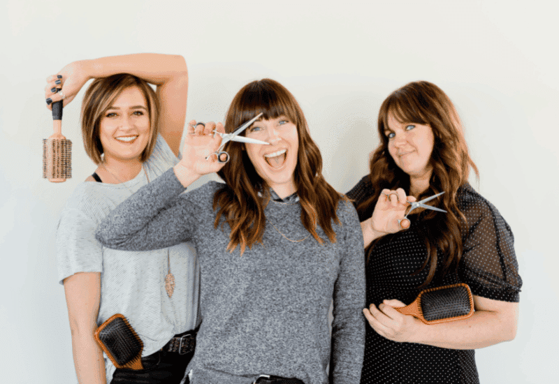 Three smiling hair stylists holding scissors and brushes in their salon